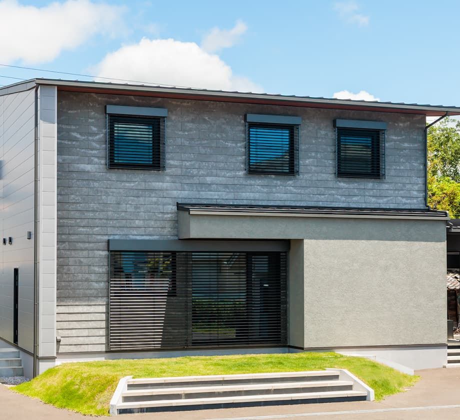 グレーの外壁と大きな窓を備えた二階建て住宅