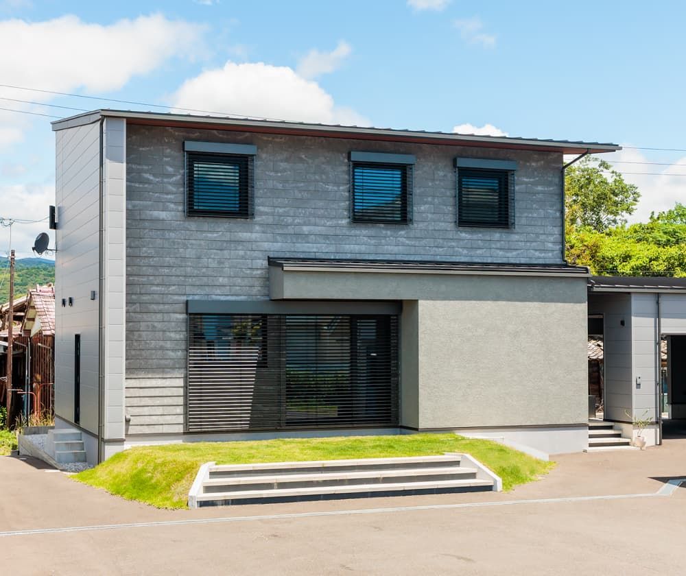 グレーの外壁と大きな窓を備えた二階建て住宅